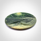 A spectacular, engraved jade disc sculpture. Hand carved in New Zealand from stunning Jade. This is a beautiful disc sculpture carved with a mountain and valley into its face. It is presented with a greywacke beach stone display stand. A beautiful sculptural piece hand carved in New Zealand.